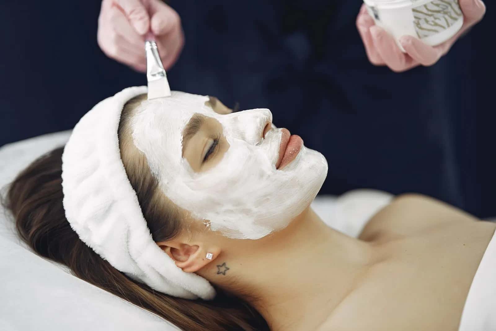 Therapist brushing a cream face mask onto a relaxed client's face