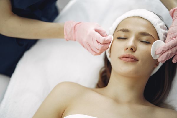 Therapist in pink gloves cleansing a client's face with cotton pads