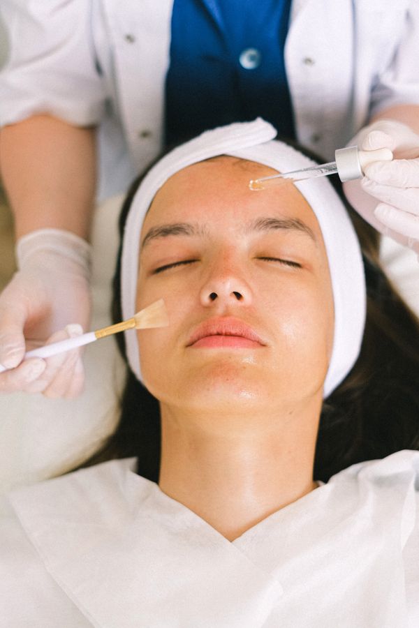 Therapist applying serum to a client's face with a dropper and a brush