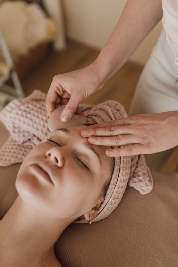 Therapist smoothing a pink gua sha stone across a relaxed client's forehead